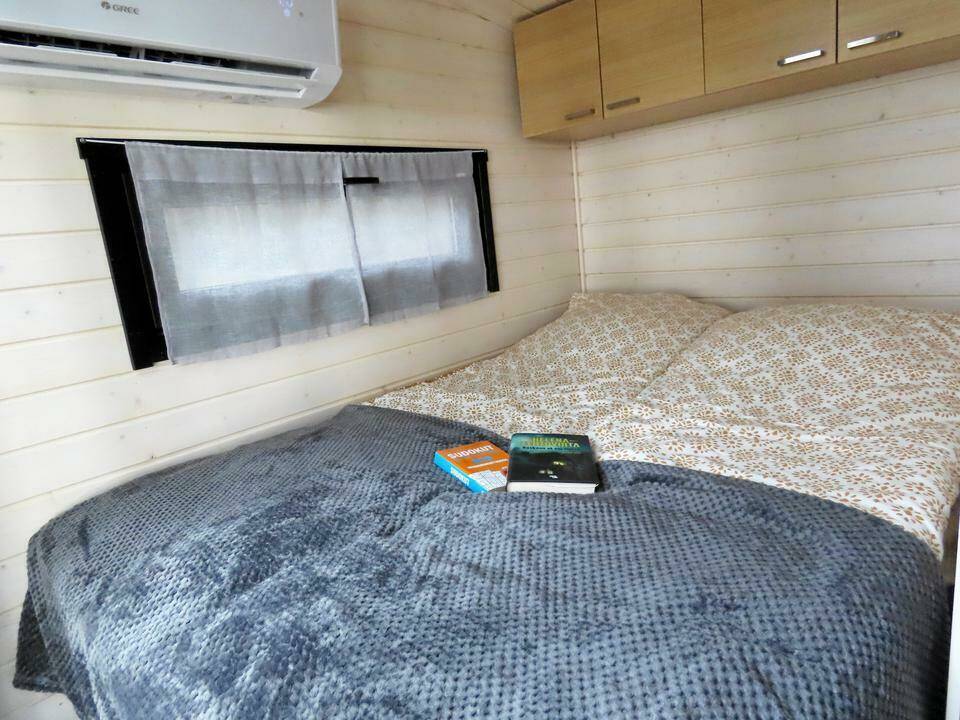 Makuuhuoneessa on parisänky, jonka päällä on harmaa peitto ja kaksi kirjaa. Ikkunassa on vaaleat verhot ja seinällä on ilmastointilaite.